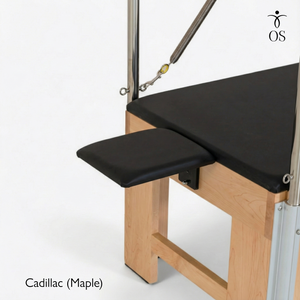 Pilates reformer with black cushioned surface and wooden base on a white background