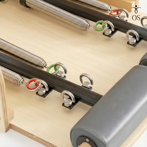 Close-up of the adjustable gear bar and spring attachment points on the Maple Timber Reformer, showing color-coded resistance springs and the carriage stopper.