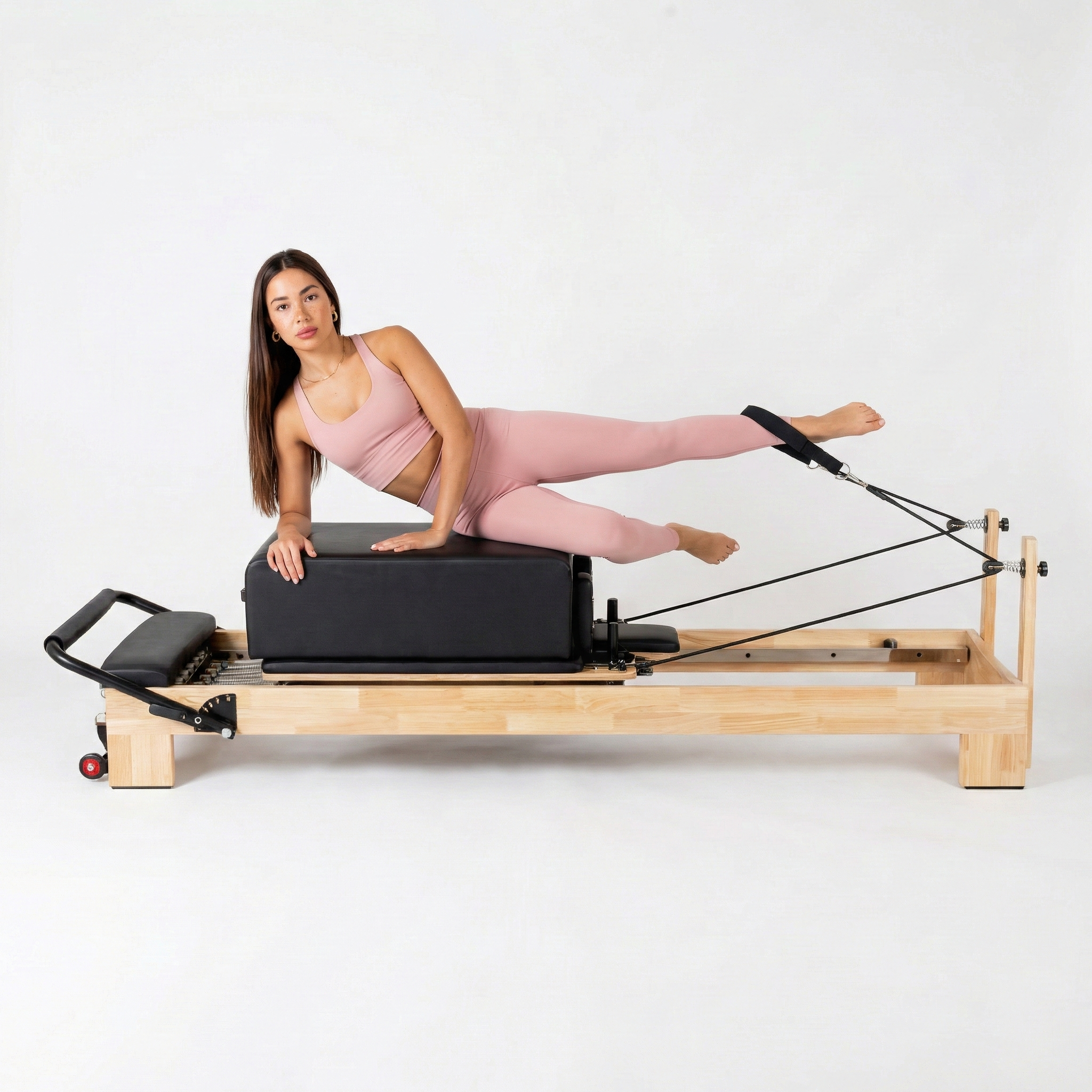 Pilates instructor performing side plank mermaid exercise on a solid oak commercial reformer to demonstrate frame stability.