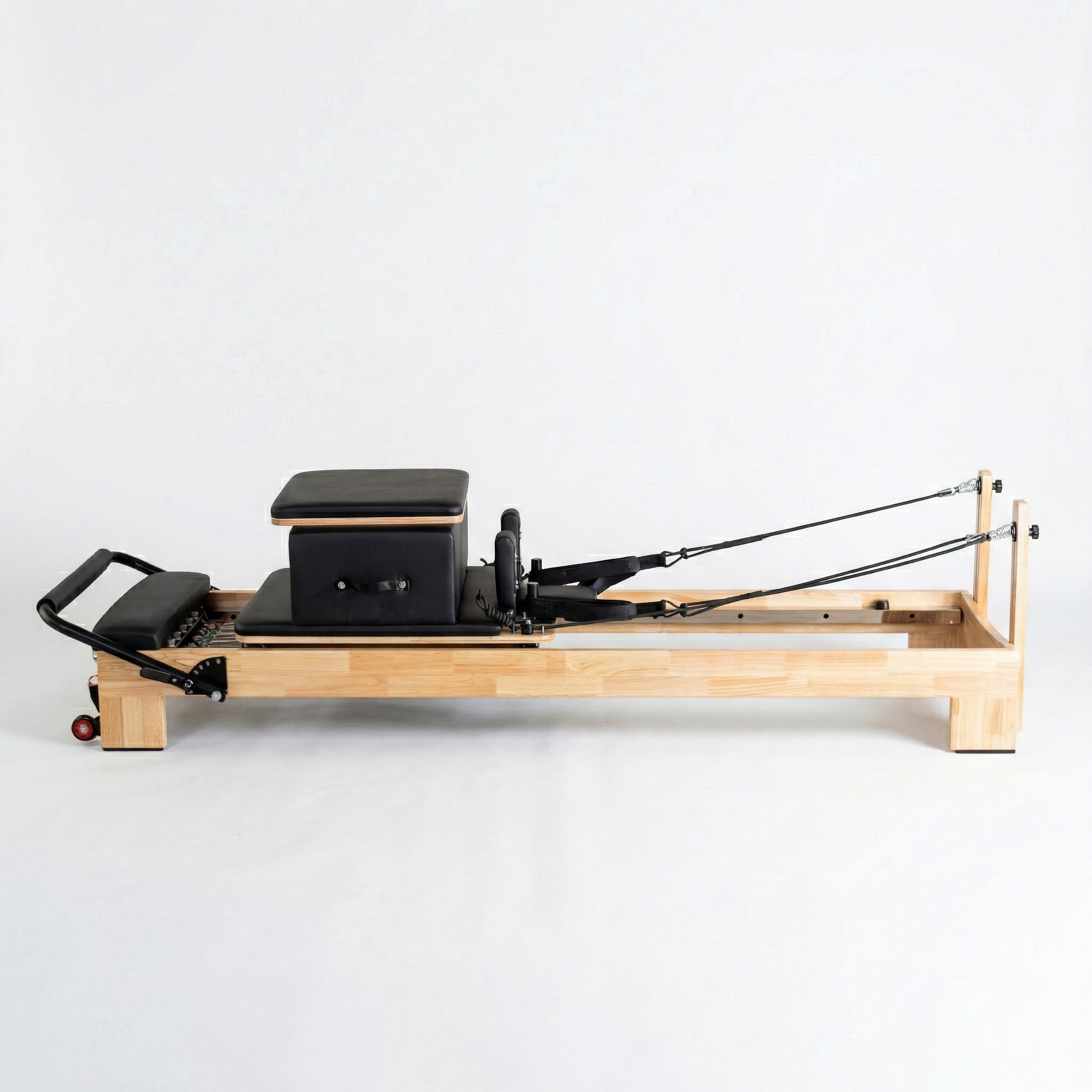Full view of The Timber Reformer by Oshun Studios made from solid oak wood, shown with sitting box and black upholstery for professional Pilates studios.