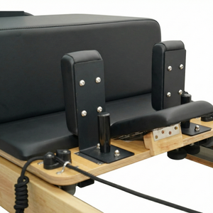 Rear view of the oak Pilates reformer showing the adjustable riser system and rope pulley mechanics.