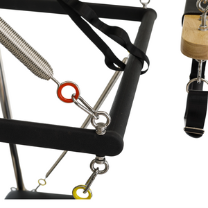 Padded black trapeze swing bar attached to color-coded resistance springs on the Timber Cadillac Tower canopy.