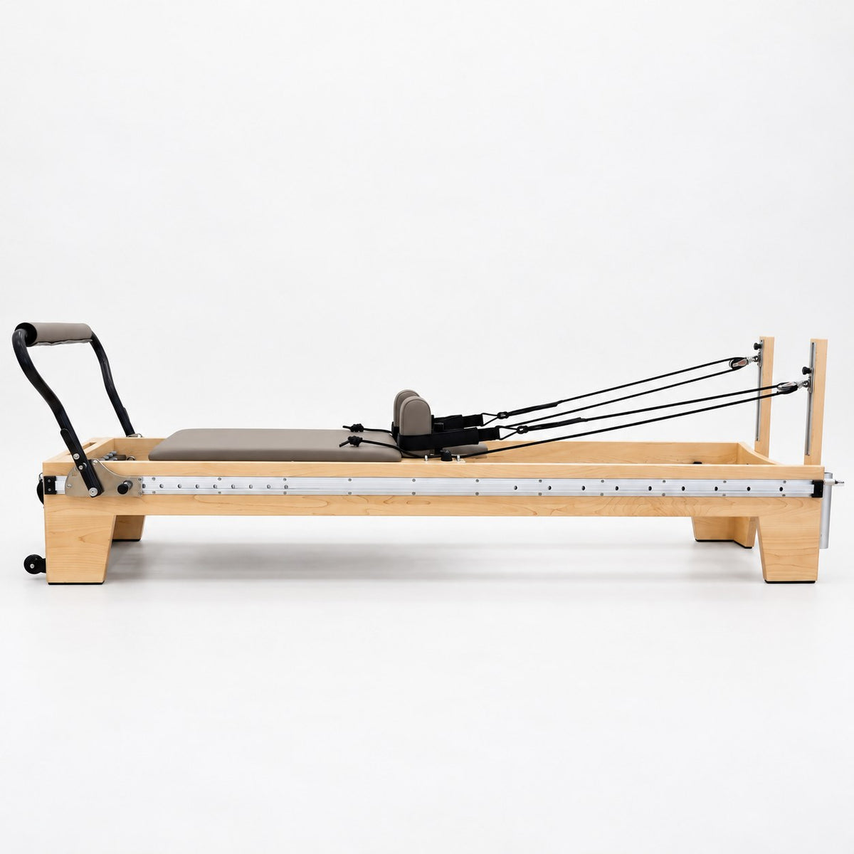 Side view of the Oshun Timber Therapy Reformer in maple, with the full-length footbar rail and rope risers