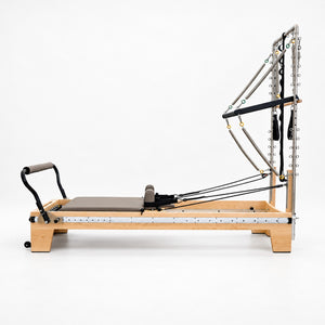 Side view of the Oshun Timber Therapy Reformer Tower Edition in maple, with the half tower, push-through bar and full-length footbar rail