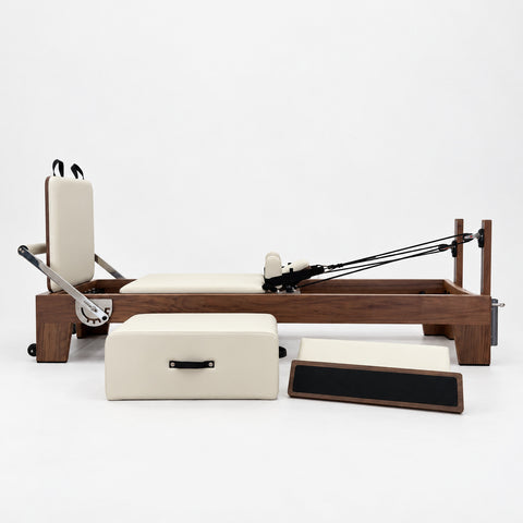 Oshun Timber Reformer in solid walnut with ivory upholstery, side view with its sitting box and jump board on a white background