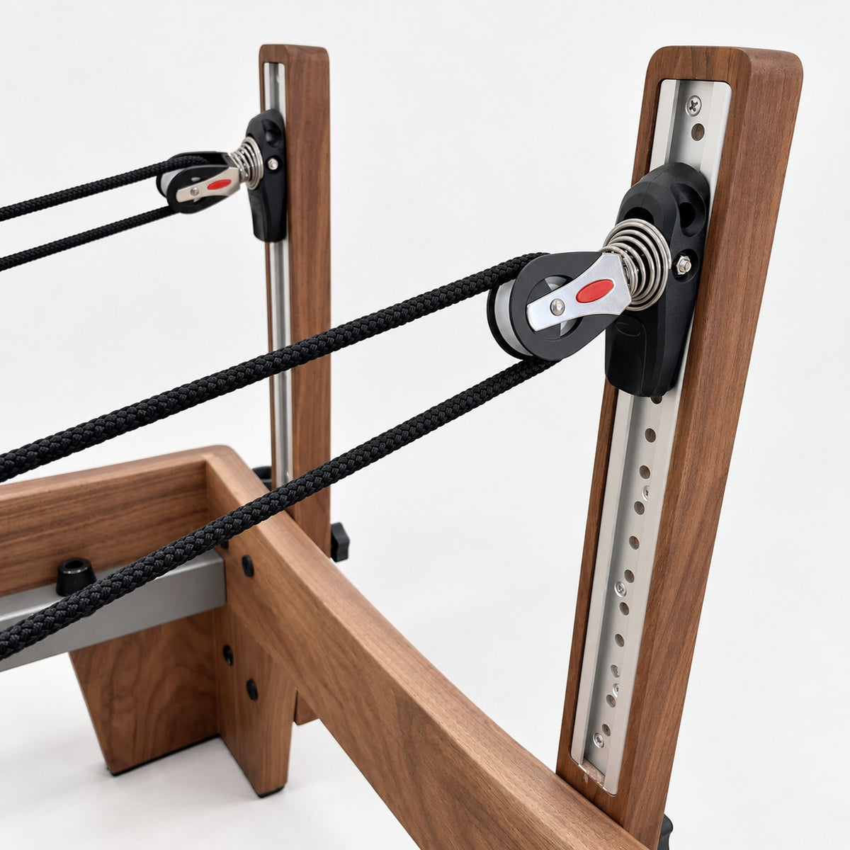 Height-adjustable rope pulleys on aluminum riser rails in the solid walnut uprights of the Oshun Timber Reformer