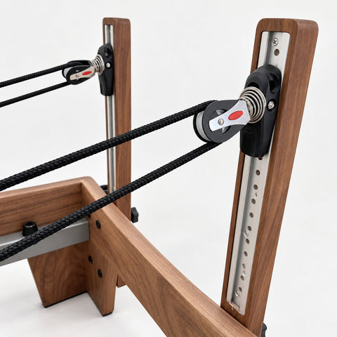 Height-adjustable rope pulleys on aluminum riser rails in the solid walnut uprights of the Oshun Timber Reformer