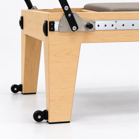 Tapered maple leg, caster wheel and footbar bracket on the aluminum rail of the Oshun Timber Therapy Reformer at Rehab Height